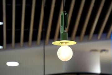 Close-up of a modern pendant light with a frosted round bulb and a green flat metal shade. The light glows softly against the backdrop of a dark ribbed ceiling.

