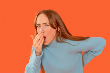 Woman has back pain, covers her mouth with one hand and holds  back with other on orange background