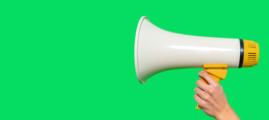 Loudspeaker held by a hand against a bright green backdrop during an announcement or rally