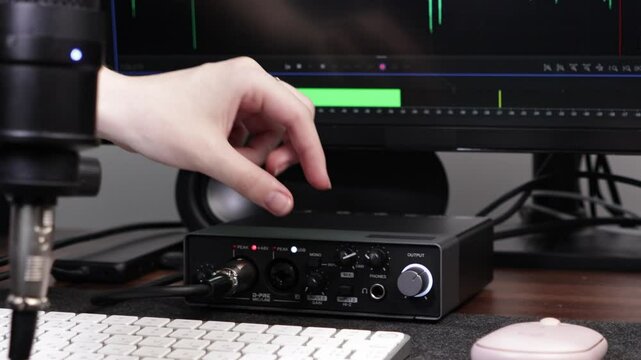 Hand adjusting gain knob on a professional audio interface, used for sound production, illustrating home studio setup and creative digital workspace
