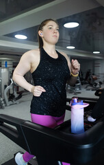 Real woman with a normal body working out on treadmill in gym. Realistic fitness and healthy weight...