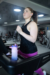 Real woman with a normal body working out on treadmill in gym. Realistic fitness and healthy weight...