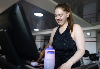 Real woman with a normal body working out on treadmill in gym. Realistic fitness and healthy weight...