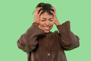 Woman expressing frustration while holding her head in a bright green background during a casual...