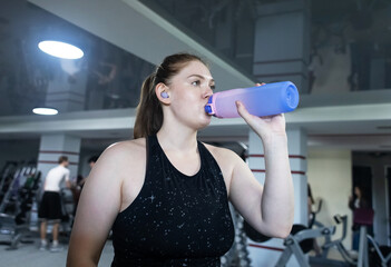 Woman tired from running on treadmill and drinking water from bottle. Complex cardio workout and...