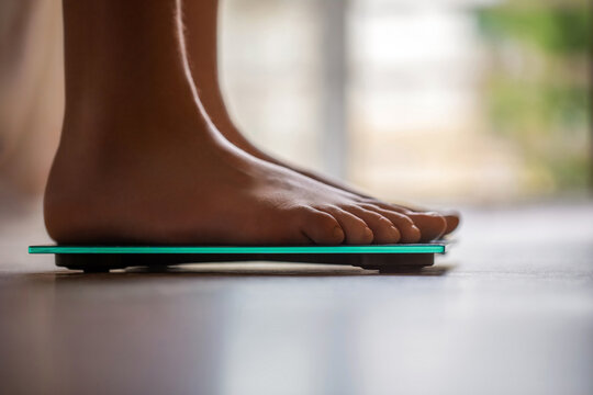 Barefoot female standing on digital weight, body fat scales with display showing. Female bare feet standing on a scales. Person standing on scale measuring weight. Health, fitness, weight, wellness