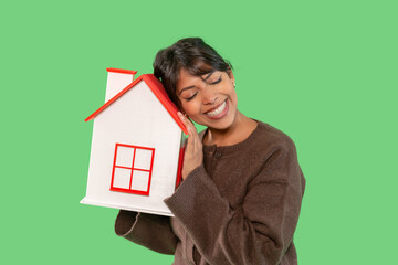 Woman happily embraces a model house symbolizing home ownership during a creative indoor photoshoot