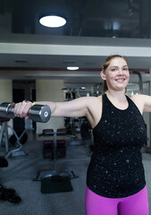 Ordinary woman in the gym doing exercises with dumbbells. Workout for weight loss. Body...