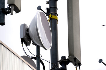 Close-up of telecommunications equipment on a metal pole against a bright, overcast sky. The setup...