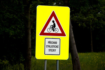 Bright yellow road sign warns of a bicycle crossing ahead. The triangular red-bordered sign...