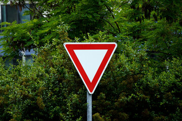 Close-up of a yield traffic sign with a white interior and red border, mounted on a metal pole. The...