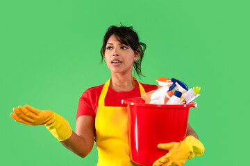 Woman in bright apron holds cleaning supplies while gesturing, ready to tackle household chores in...