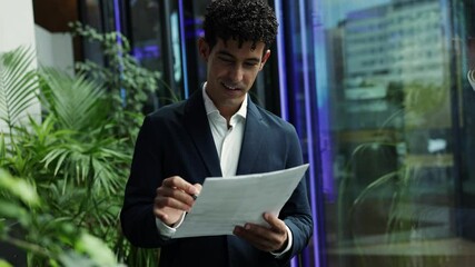 Young businessman reviewing and signing documents in a modern office with plants - Powered by Adobe