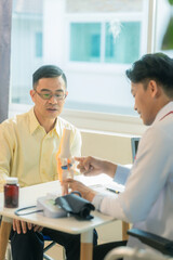 Senior man consults with doctor about joint pain and mobility problems in clinic. Asian male doctor and patient talking in hospital office. Healthcare services.
