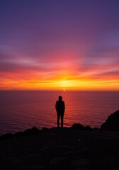 Fototapeta premium Silhouette of Person Watching Vibrant Sunset Over Ocean