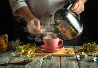 A person pours steaming water from a kettle into a pink cup while using a strainer to steep dried...