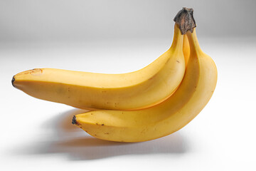 Three ripe bananas arranged on a plain white background, showcasing their yellow skin and slight blemishes.