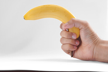 A hand holds a ripe yellow banana, mimicking the shape of a handgun, against a white background.