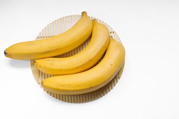 Three ripe bananas arranged on a light brown bamboo placemat against a white background.