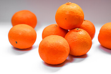 A group of bright orange citrus fruits, stacked and scattered on a white surface, creating a vibrant and fresh display.