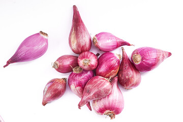 A cluster of elongated, reddish-purple shallots scattered on a bright white surface, showcasing their unique shape and color.
