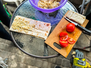 Cook preparing lavash with tomatoes and cheese filling on glass table outdoors