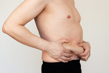 An adult Caucasian man showing fat folds on his stomach with his hands. Obesity, overweight.