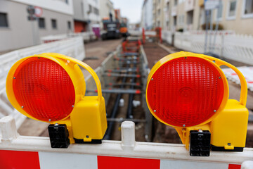 Urban street excavation with visible pipelines and safety barriers. Red warning lights and construction fencing mark the site in a residential area under infrastructure repair