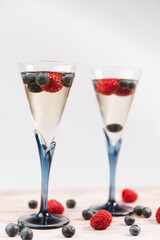 Champagne glasses with fruits,Elegant champagne glasses filled with sparkling wine and fresh fruits inside, surrounded by scattered berries on a light background. Festive and refreshing composition 