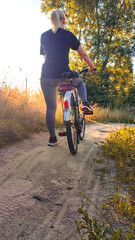 Woman riding cruiser bike riding in remote area on sunset. Back view. Cyclist girl biker enjoys...