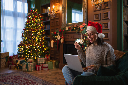 Merry Christmas. Young woman shopping online with laptop paying with gold credit card for Christmas gifts. Girl buying on Internet enter credit card details enjoying winter holidays at home