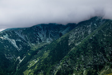 Steep green mountains rise into rocky peaks shrouded in drifting mist and cloud. The dense...