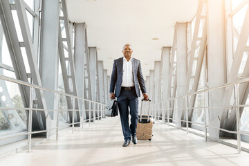 Businessman walking through airport pulling suitcase with relaxed but purposeful stride. Holding...