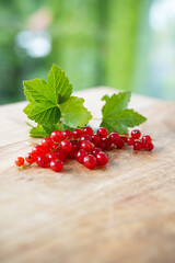 Bunch of ripe red currants with green leaves on wooden table against  light background. Vertical close-up of seasonal healthy fruits. Space for text.