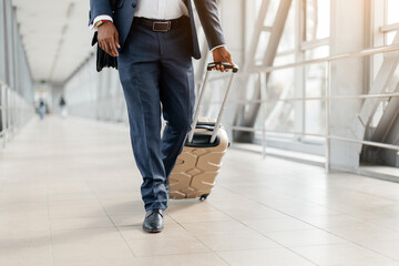 Closeup of businessmans legs walking through airport with a rolling suitcase. Male dressed in navy blue suit and formal shoes, concept of mobility, style, and business travel