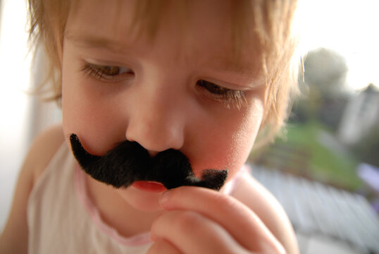 A young child dressing up and playing with a false moustache