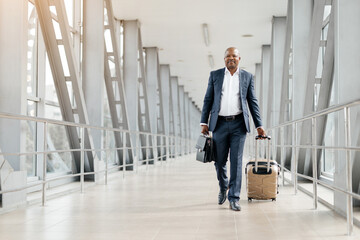 Businessman walking forward in airport corridor with suitcase and briefcase. Looking straight ahead...