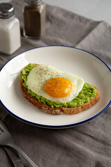 Homemade Avocado Toast with Egg on a Plate, side view.