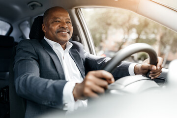 Black businessman driving car and smiling while holding steering wheel, hands firmly positioned....