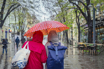 Rear view of two women under one umbrella. Two people going under colorful umbrella on rainy city...