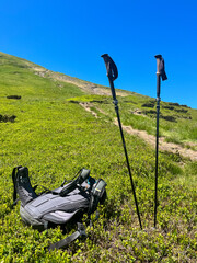Backpack and trekking poles on a sunny mountain trail.