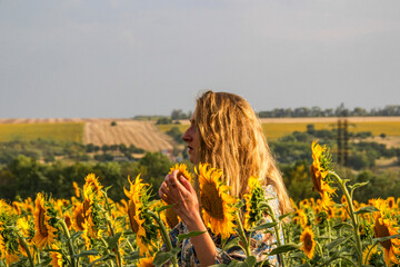 blonde woman standing in a field of yellow sunflowers, profile, waist-length portrait, looking to the side, sky and forest background, teenager, bright flowers, large petals, summer field, medium shot