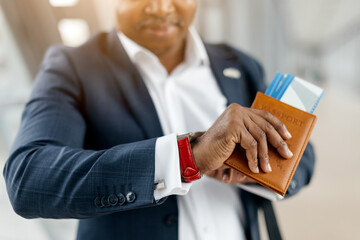 Closeup of black businessman checking time on watch while holding passport. Sharp and detail...