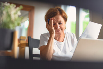 Sad frustrated senior woman pensioner having depressed look, holding hand on her face, calculating...