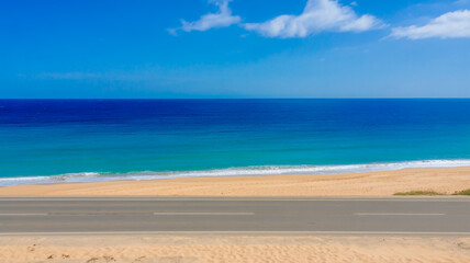 Fototapeta premium A wide-angle photograph of a pristine beach coastline with a straight asphalt road in the foreground