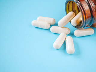 White antibiotic capsule pills spread out of pill amber glass bottle on blue background.