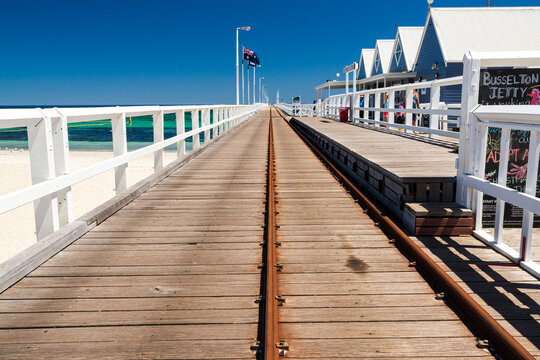 A long  Jetty with train lines leading to a distant horizon with a clear blue sky