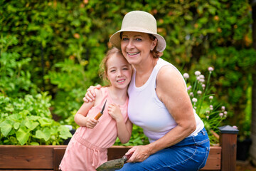 grandmother and granddaughter digging soil with gardening tools in yard