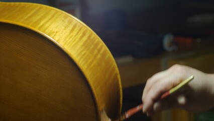 Skilled craftsman carefully varnishing wooden cello component, surrounded by specialized lutherie...