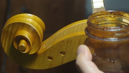 Luthier applying varnish with a brush on a cello part in a traditional workshop, highlighting the...